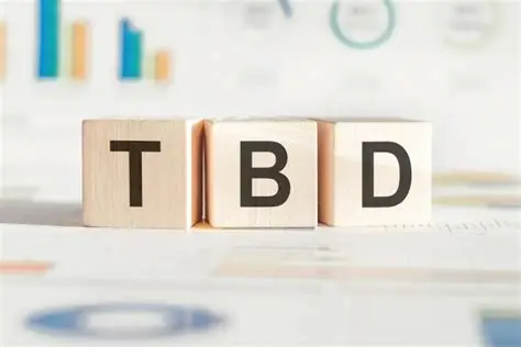 Wooden blocks spelling TBD placed in front of a blurred background of colorful business charts.