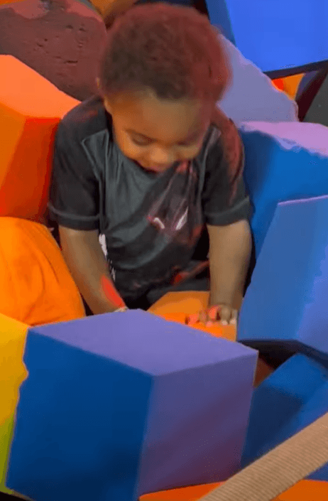 Young child with dark curly hair playing in a pit of colorful foam blocks.