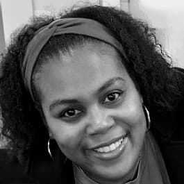 Smiling woman with curly hair, headband, and hoop earrings in a black and white portrait.